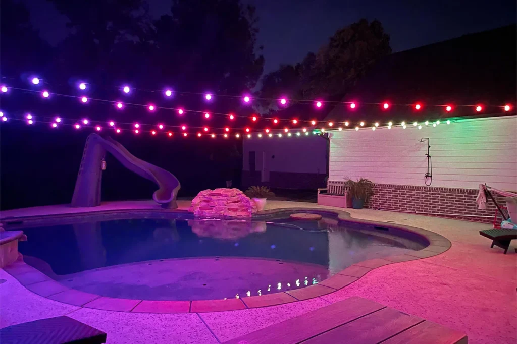 Backyard pool at night under multicolor globe string lights