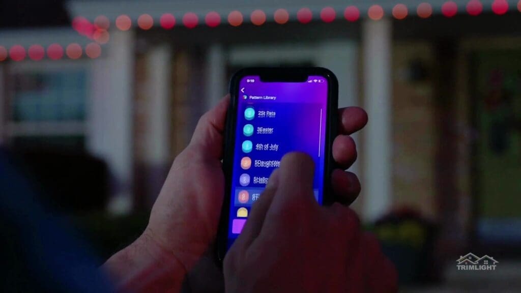 Hand holding a phone with the Trimlight app open in front of a lit home